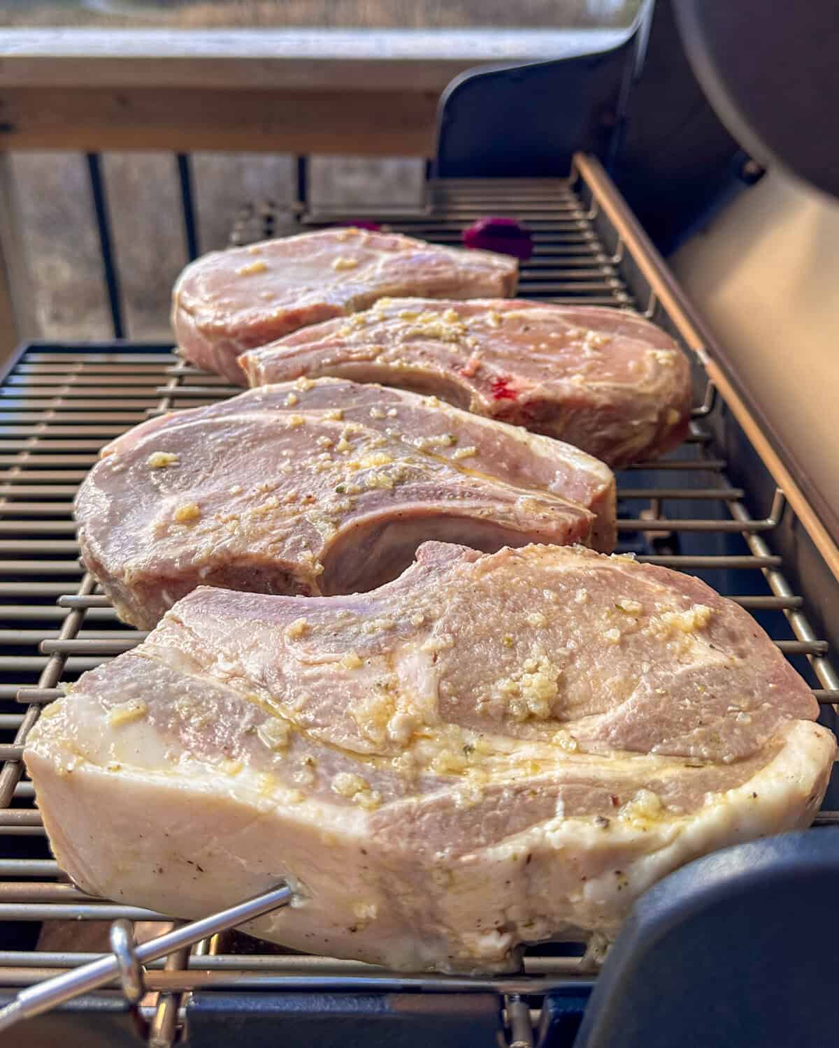 Four thick-cut pork chops on a smoker with a temperature probe inserted in the thickest part.
