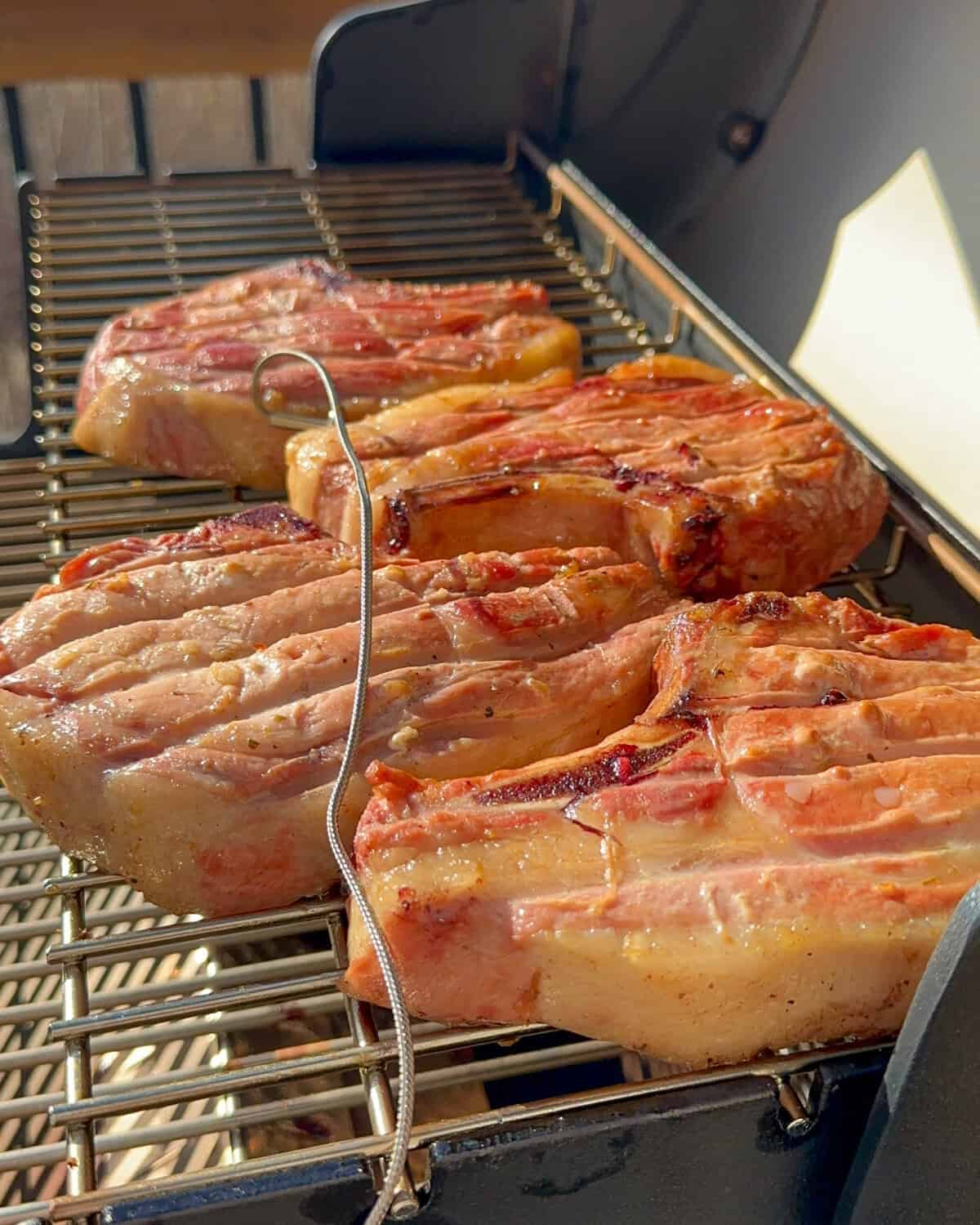 Four thick-cut, golden brown pork chops with grill marks on the pellet grill (smoker).