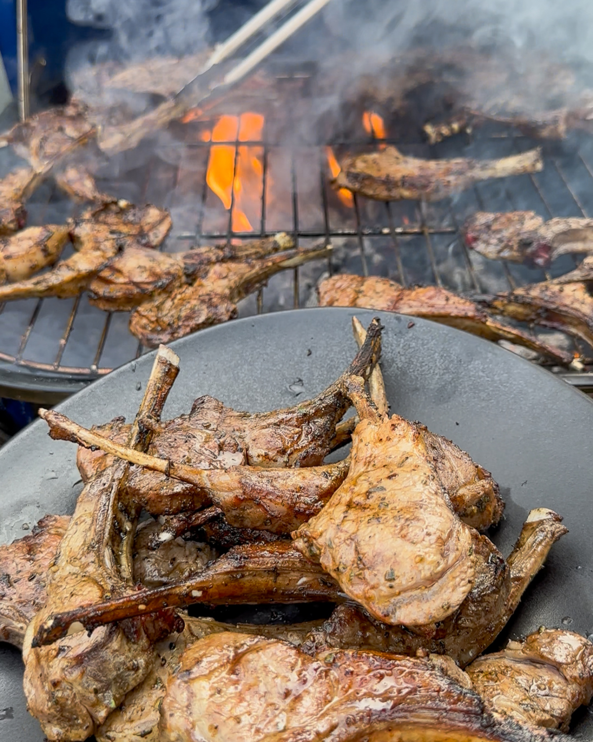 Lamb chops coming off a BBQ with flames onto a platter.