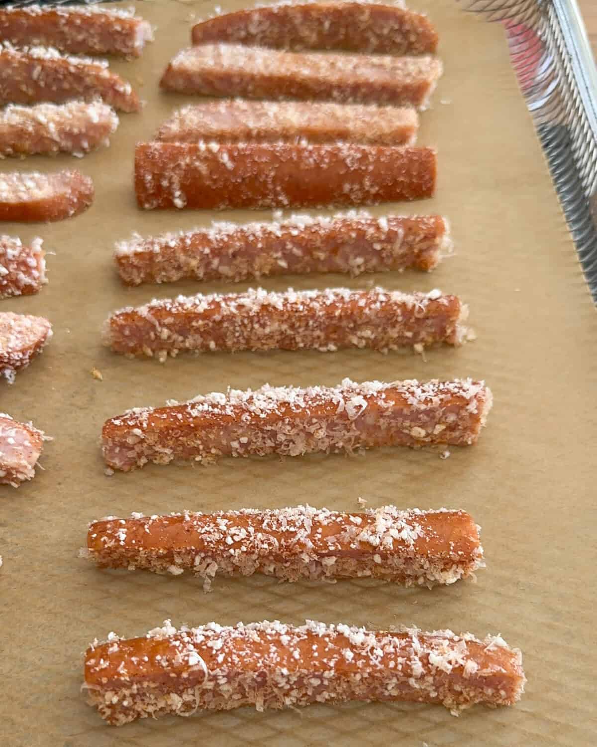 Coated kolbassa strips in a single layer on parchment paper in the air fry basket.
