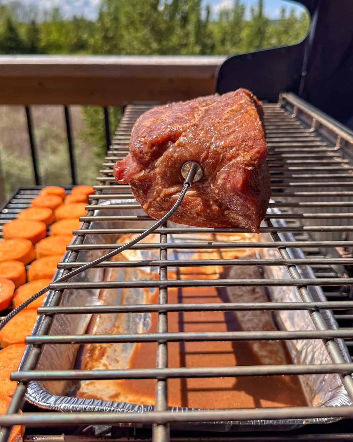The marinated coppa is place on the top rack of the grill with and temperature probe inserted and a water tray below.
