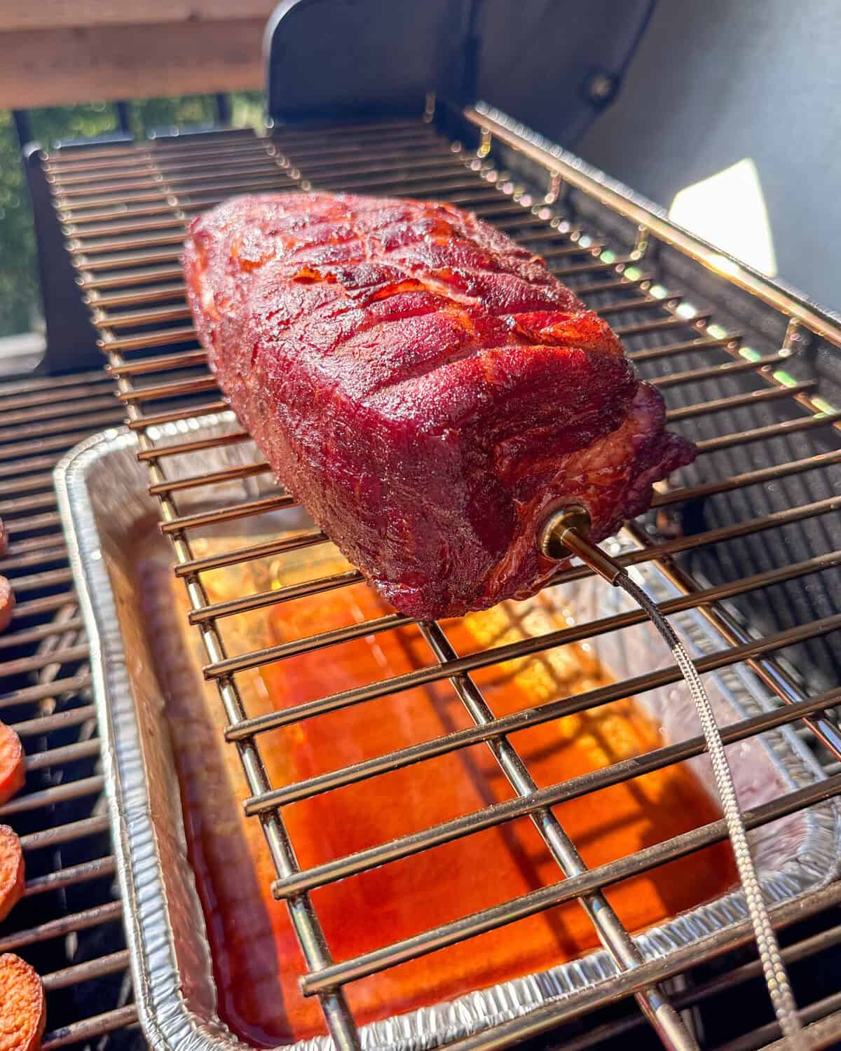 A smoked char siu pork coppa on the smoker with a glossy and caramelized crust.