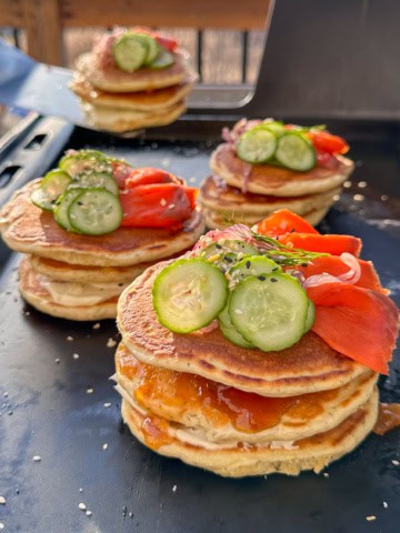 Four stacks of Lemon Dill Pancakes with Smoked Salmon and Mango Chutney on an outdoor griddle.