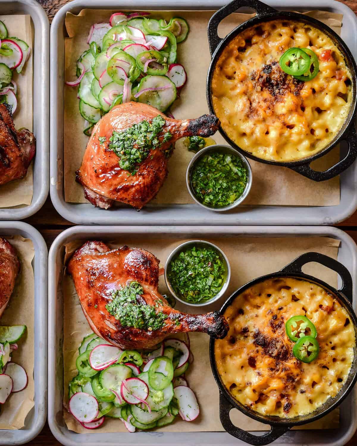 Two trays each with a smoked duck leg, served with a Charred Scallion Chimichurri, mac & cheese, and a cucumber salad.