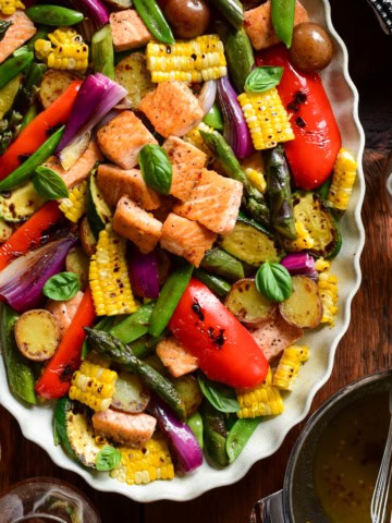 A warm salad with charred corn, salmon, potatoes and a variety of veggies on a platter.