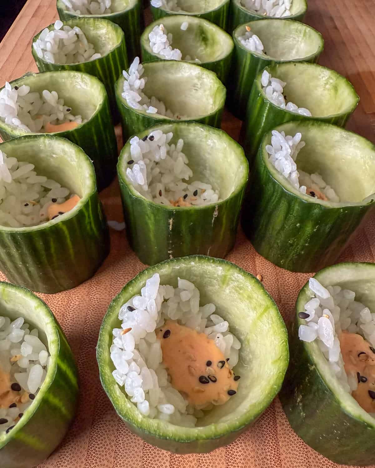 Add a dollop of sriracha mayo and sprinkle sesame seeds into each cucumber cup.