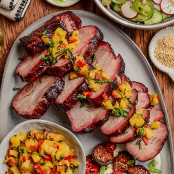 Slices of smoked char siu pork with a pineapple relish overtop and served with a cucumber salad and sweet potatoes.