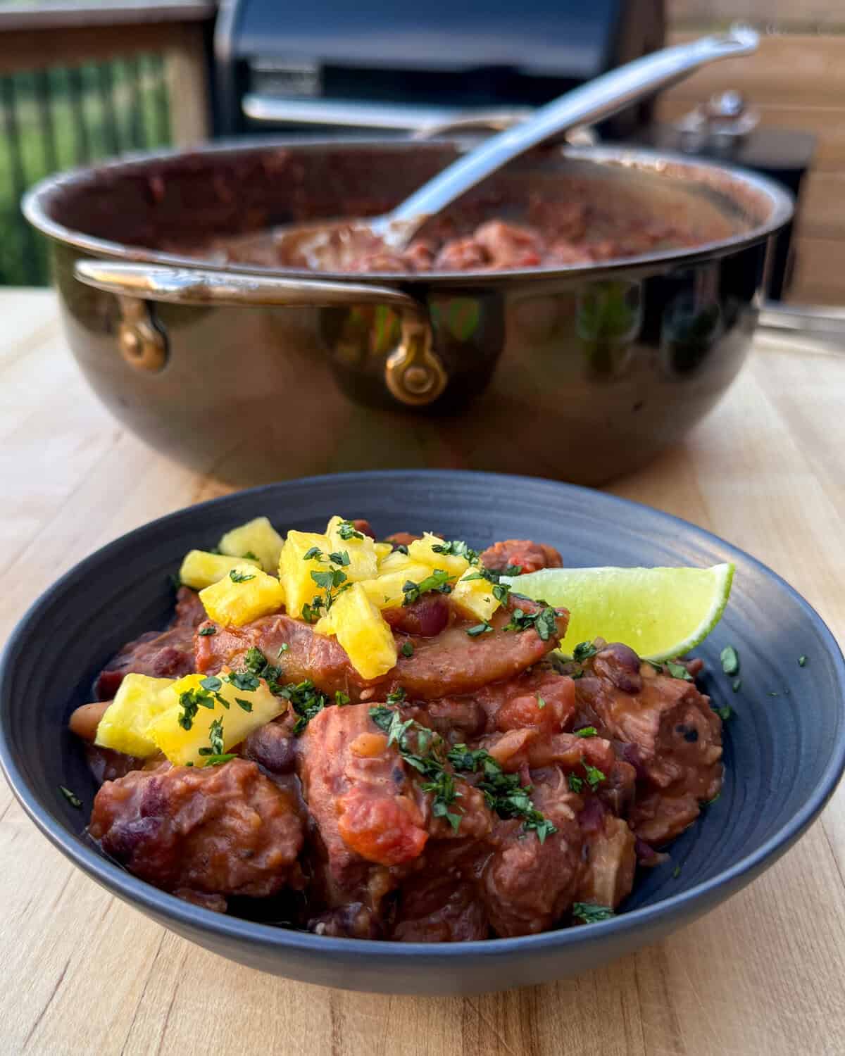 A plated bowl of Caribbean baked beans topped with pineapple, parsley and  a lime wedge.