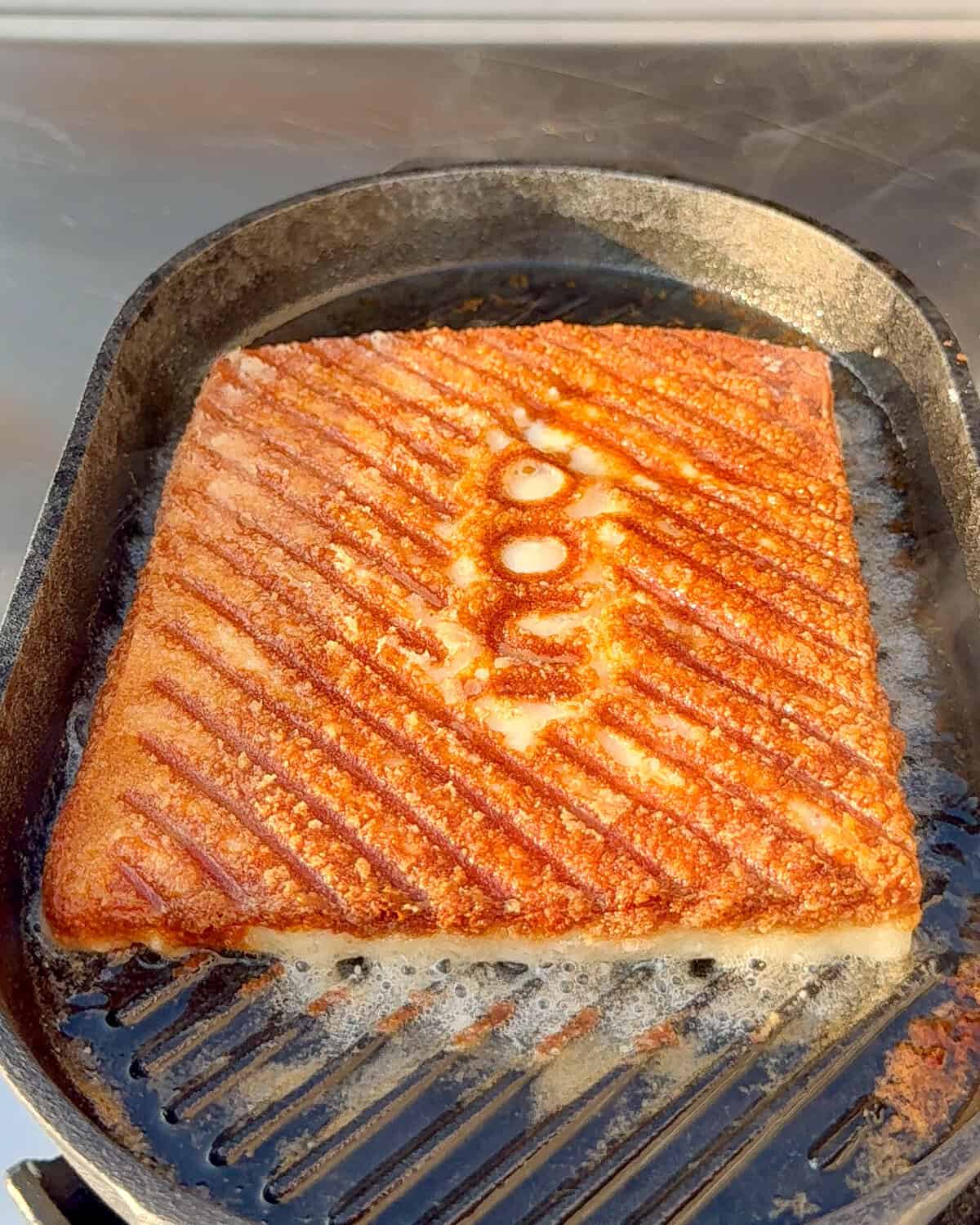 A crispy piece of Greek fried cheese with ridges and the Ooni logo embossed in the cheese.