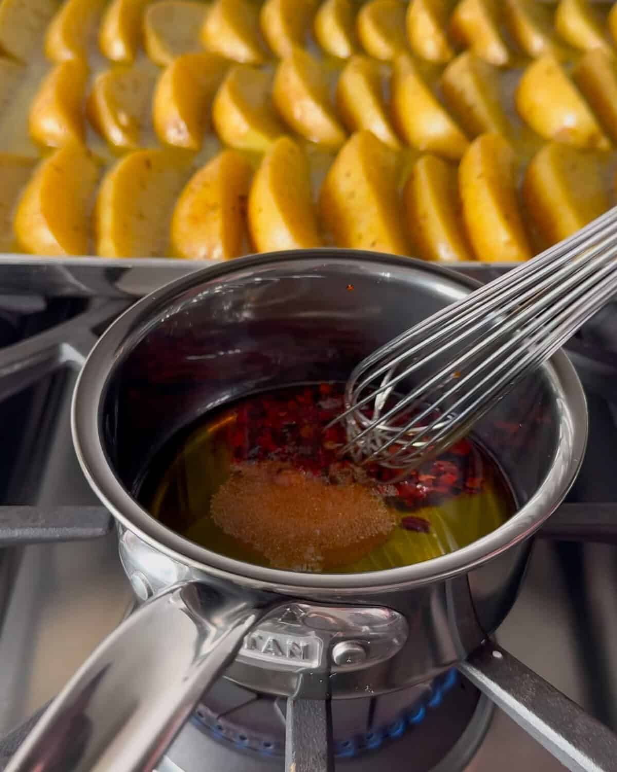 A pot of chili crisp drizzle with lemon potato wedges in the background.