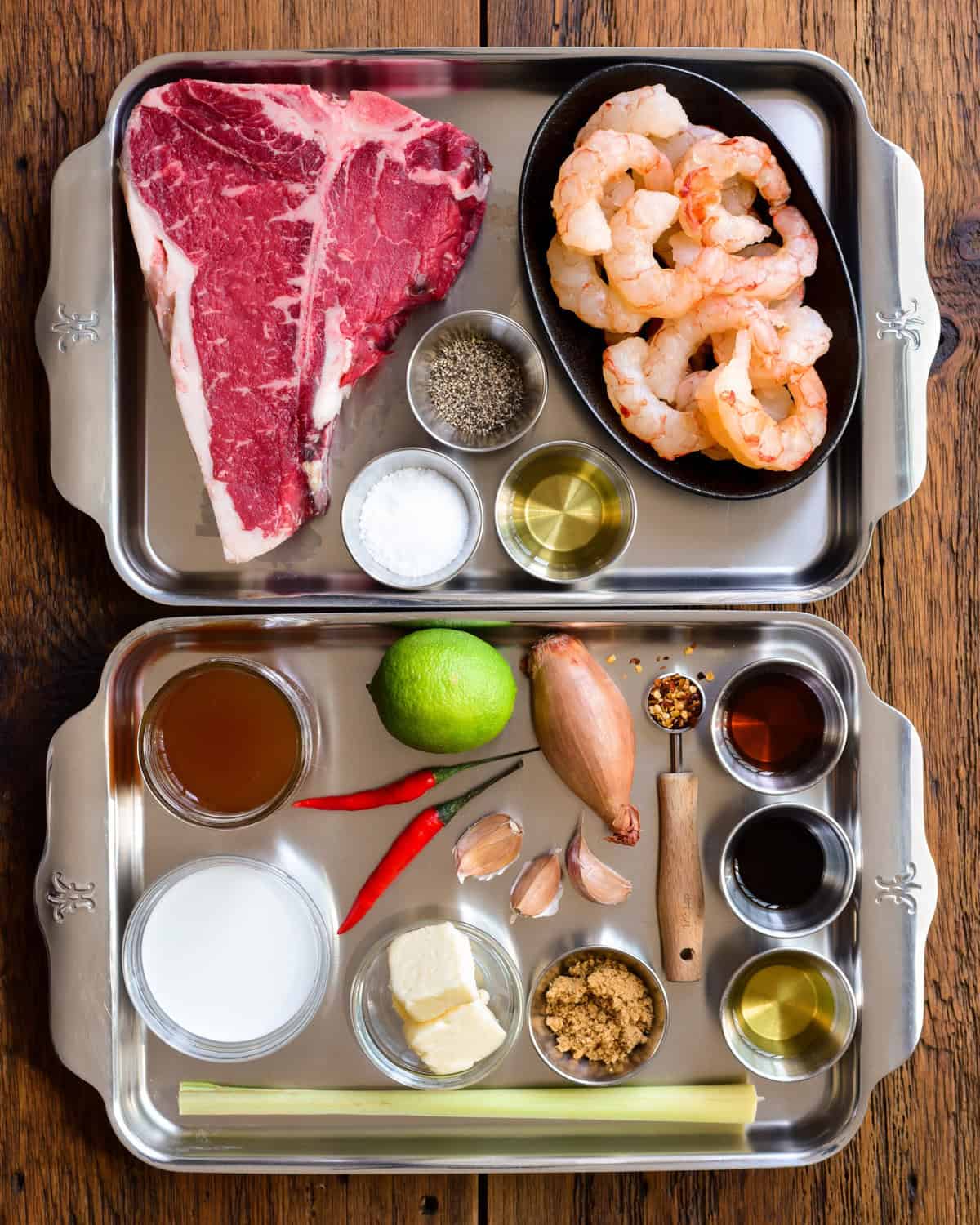 Ingredients for a grilled steak and shrimp recipe on two trays.