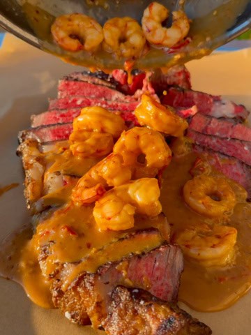 A grilled steak and shrimp image with the shrimp sauce getting poured over the steak.