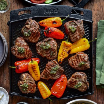A cast iron skillet with Greek lamb chops and blistered peppers.