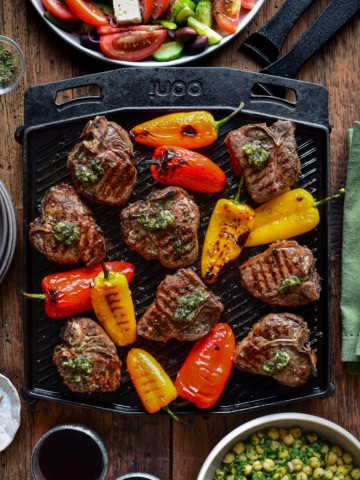 A cast iron skillet with Greek lamb chops and blistered peppers.