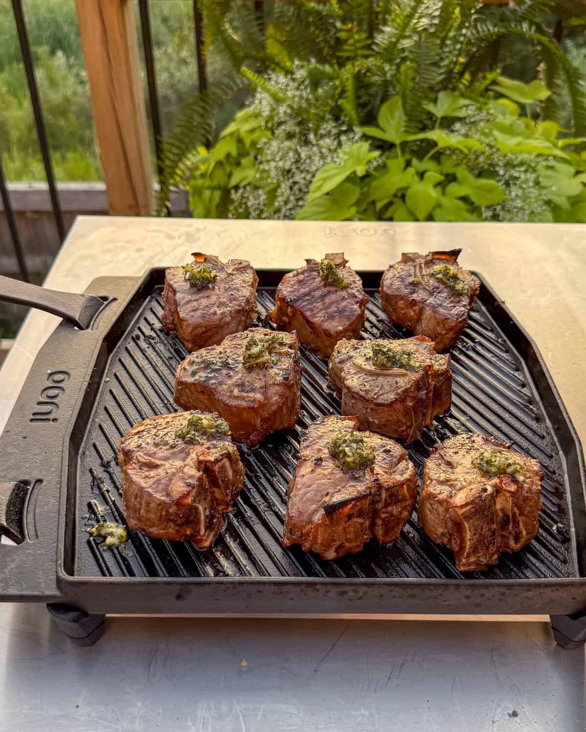 Grilled Greek lamb chop loins with sauce on an Ooni cast iron grill pan.