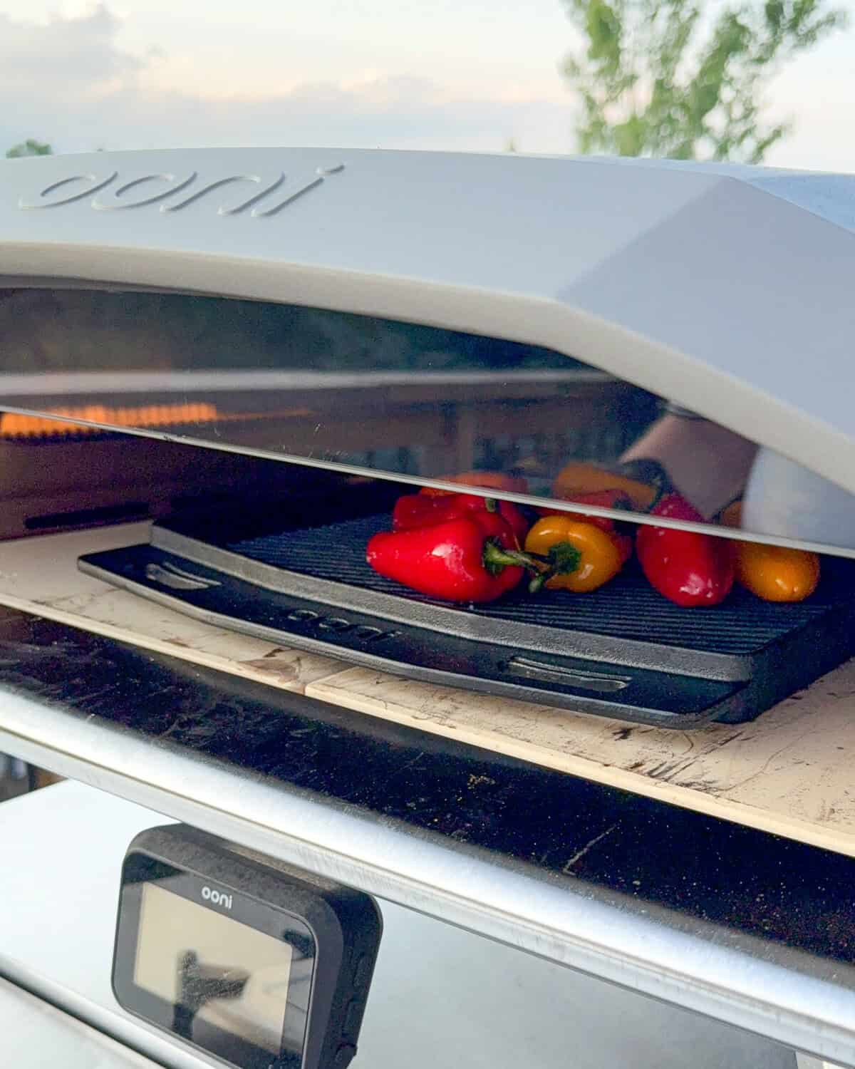 Peppers blistering in an Ooni oven on a cast iron grizzler pan.