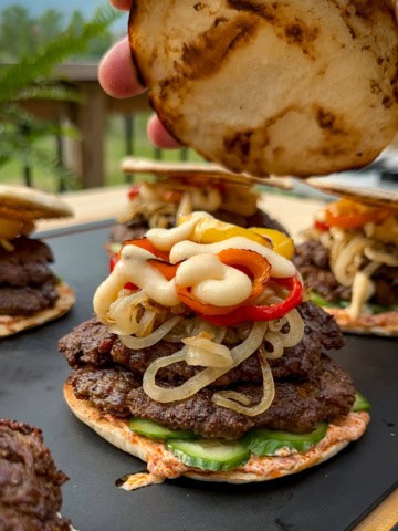 A double patty shawarma spiced lamb smash slider topped with onions, peppers and toum. The lid is being placed on the burger.