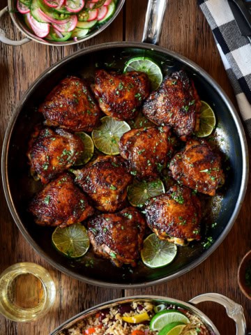 A skillet with sticky chicken thighs and lime slices.