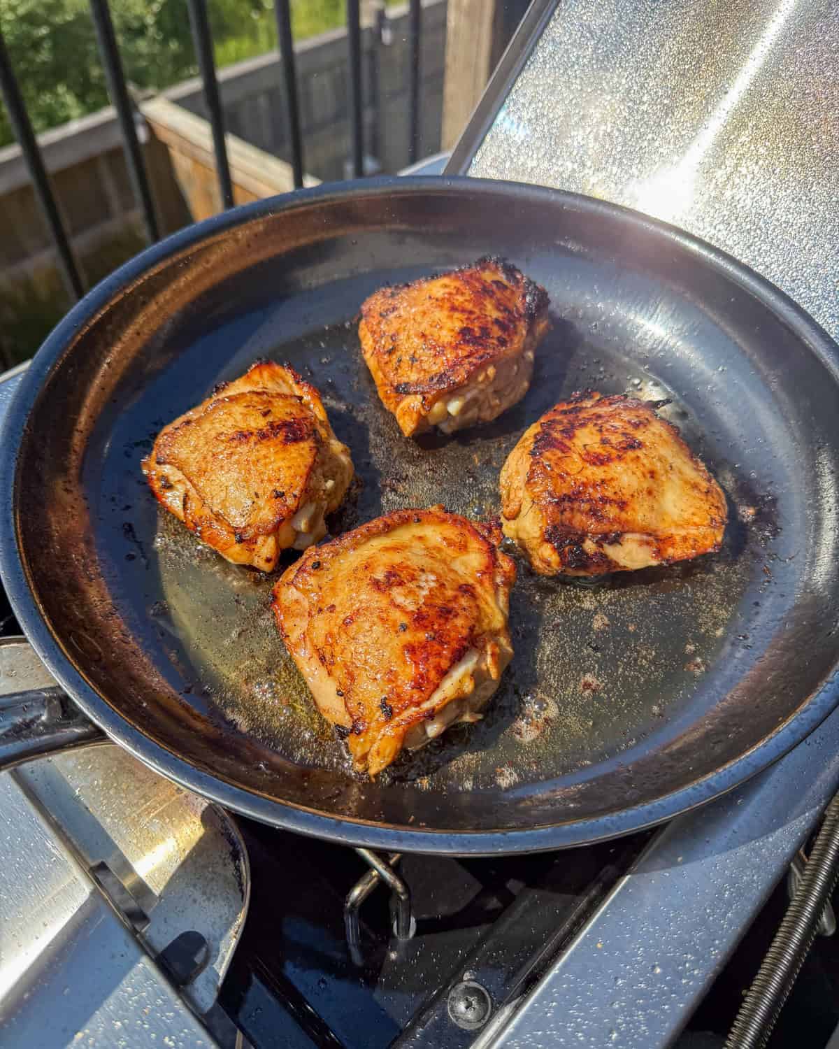 Four chicken thighs searing in a skillet, bone side down.