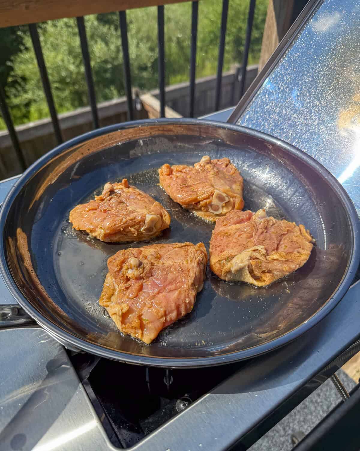 Four chicken thighs searing in a skillet, skin side down.
