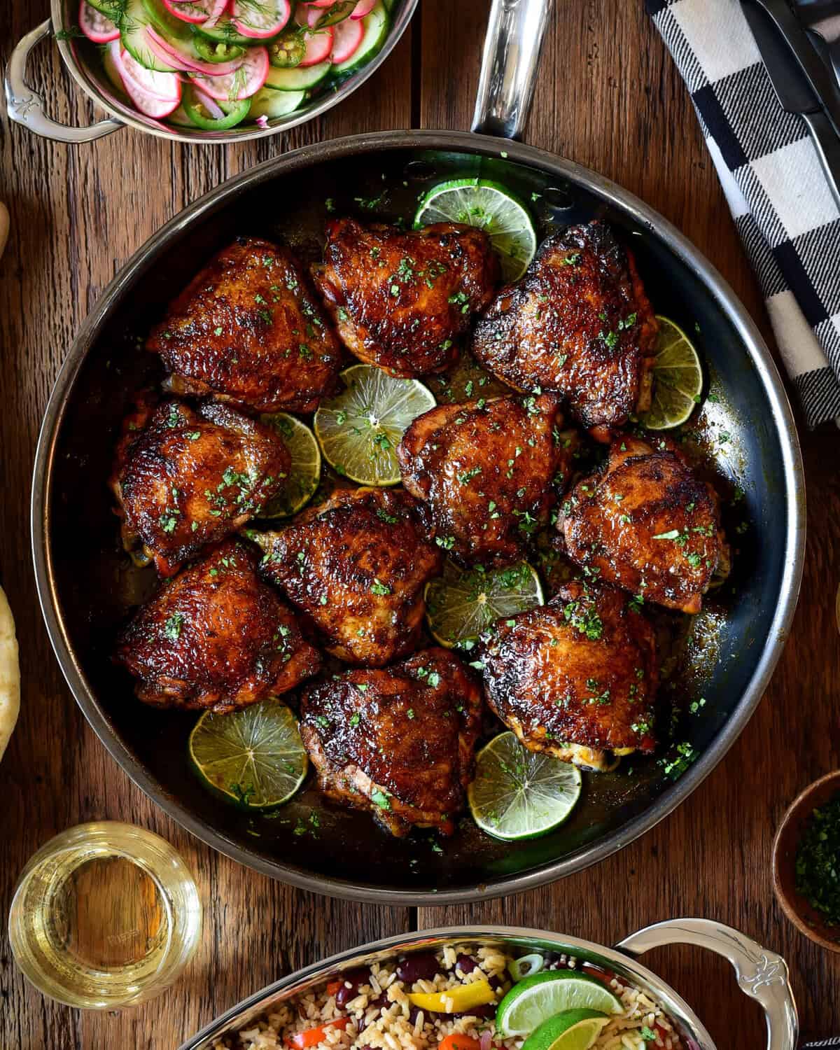 A skillet with sticky chicken thighs and lime slices.