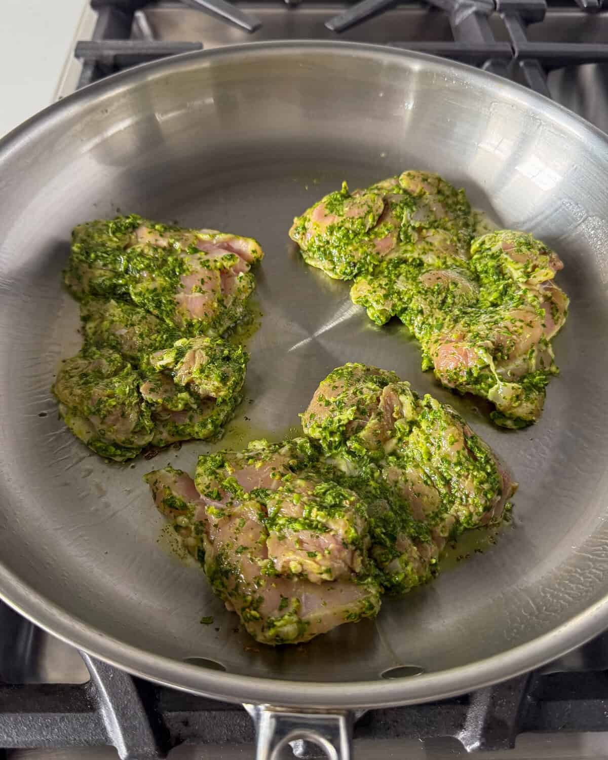 Three chicken thighs marinated in a jalapeno cilantro sauce getting seared in a pan.