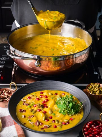 A copper pot filled with a squash soup with gnocchi and spinach.