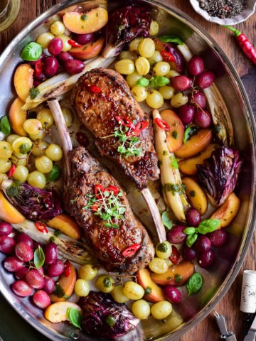A pan of Diavola Veal Chops with Chili Apple Cider Glaze served with roasted grapes and peaches.