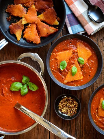 A pot of roasted red pepper tomato soup. Two bowls of soup served with three inside-out grilled cheese dumplings and fresh basil.