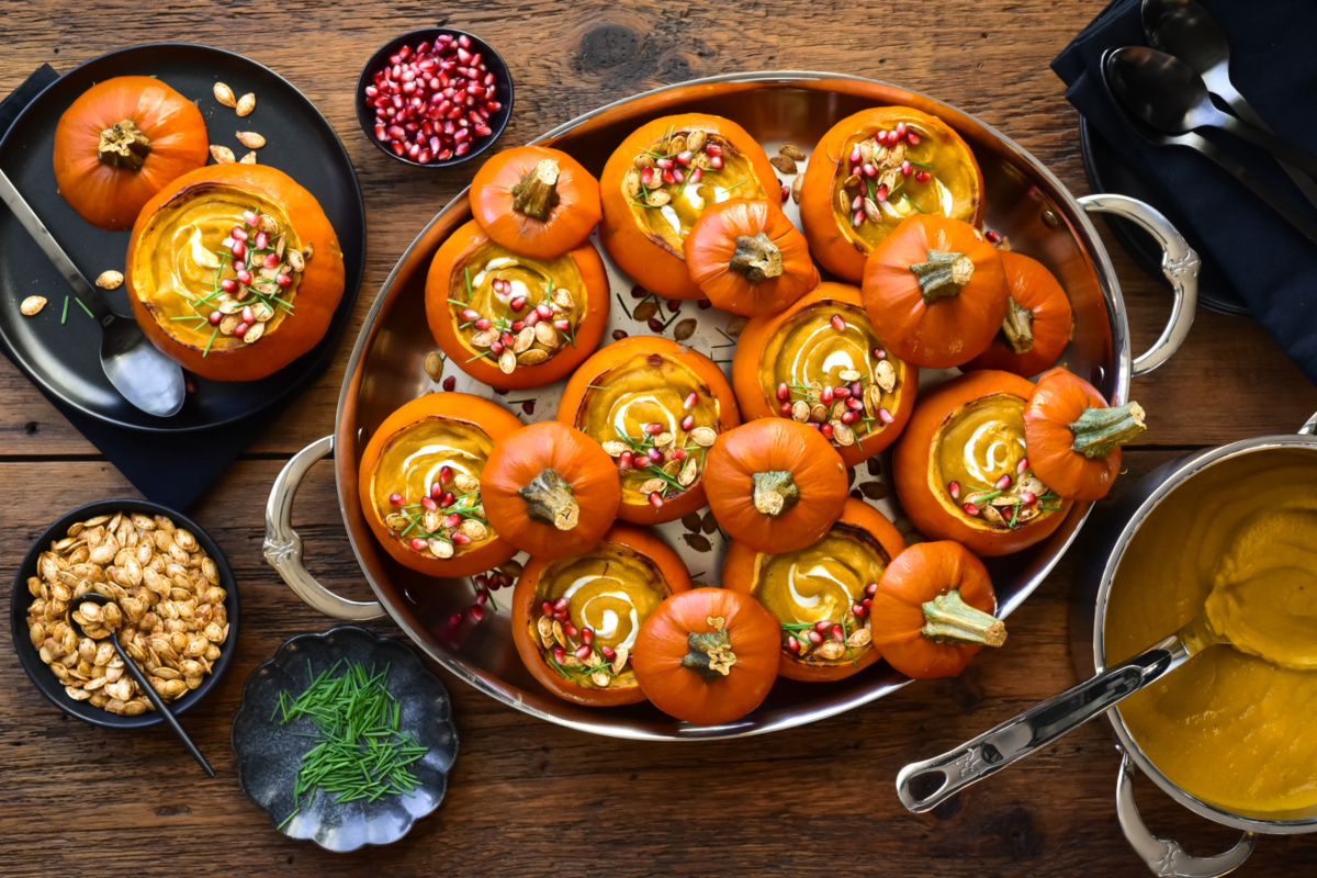 Pumpkin soups served in mini pumpkins and topped with pumpkin seed, arils, yogurt and chopped chives.