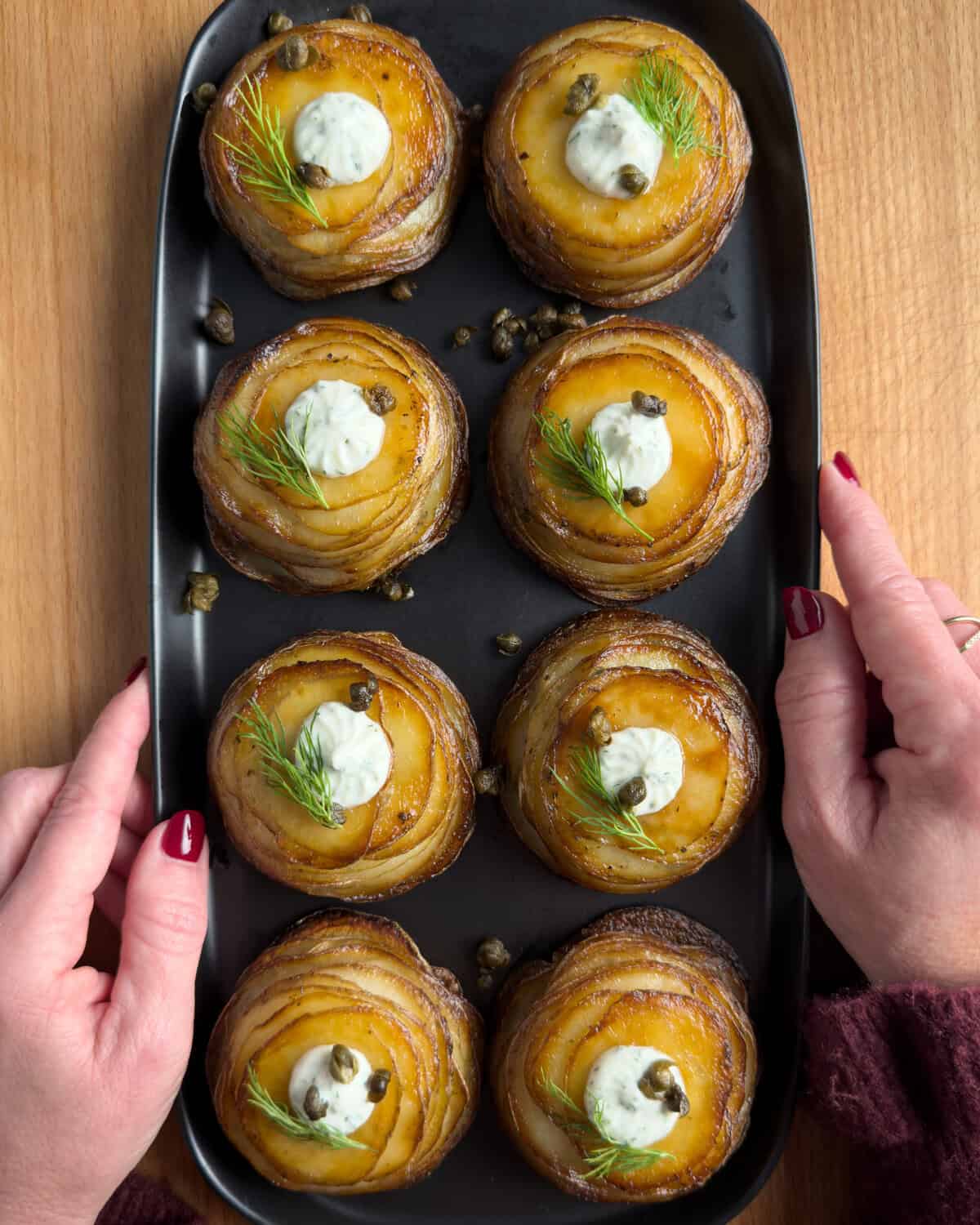 Eight potato stacks on a black platter with someone holding it.