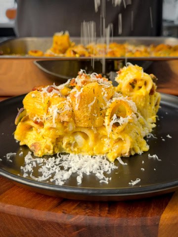A plated portion of a carbonara pumpkin pasta bake with Parmesan shavings.