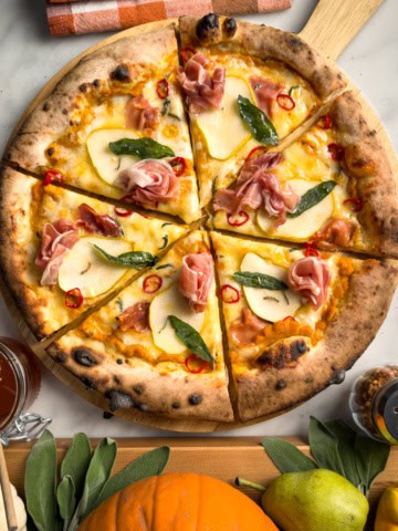 A pumpkin pear pizza with prosciutto, sage, chilis and hot honey sliced into six pieces.