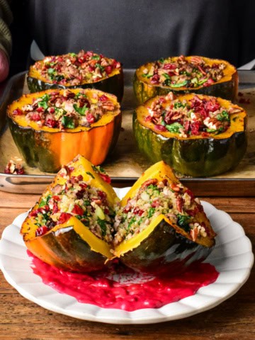 A plated & cut in half turkey quinoa stuffed acorn squash topped with cranberries, pecans, sitting on a swoosh of cranberry puree.