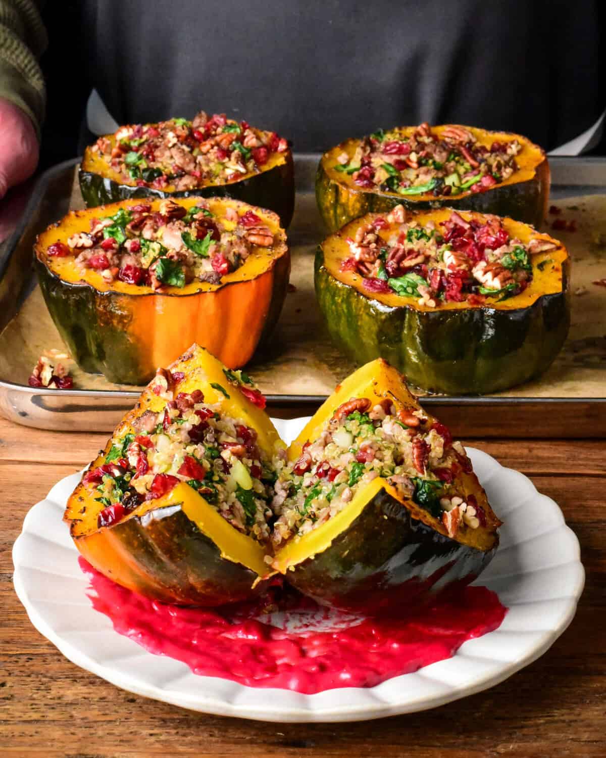 A plated & cut in half turkey quinoa stuffed acorn squash topped with cranberries, pecans, sitting on a swoosh of cranberry puree.