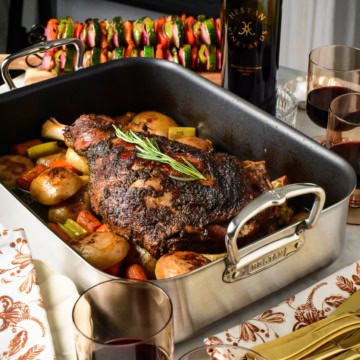 A Slow Roasted Greek Lamb Shoulder with Roasting Pan Potatoes, and served with red wine and vegetable skewers.
