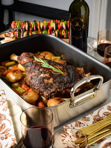 A Slow Roasted Greek Lamb Shoulder with Roasting Pan Potatoes, and served with red wine and vegetable skewers.