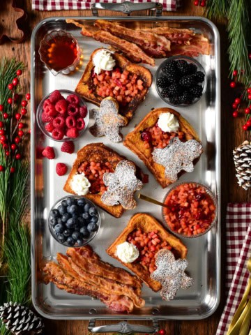 Gingerbread French Toast with Apple Cranberry Compote served with fresh berries and bacon. Topped with whipped cream and dusted with icing sugar.