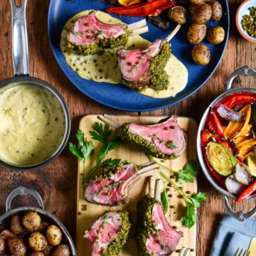 A sliced herb-crusted rack of lamb with peppercorn sauce and a plate served with potatoes and veggies.