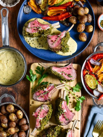 A sliced herb-crusted rack of lamb with peppercorn sauce and a plate served with potatoes and veggies.