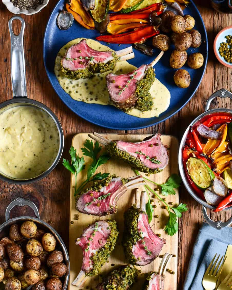 A sliced herb-crusted rack of lamb with peppercorn sauce and a plate served with potatoes and veggies.