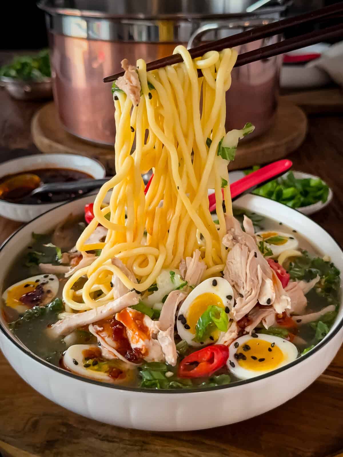 A noodle pull from a bowl of ginger chicken ramen soup with bok choy, ramen-style noodles and jammy quail eggs.