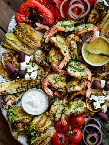 A platter with a butterflied grilled shrimp salad with grilled veggies, and served with a Lemon-Dijon Dressing.