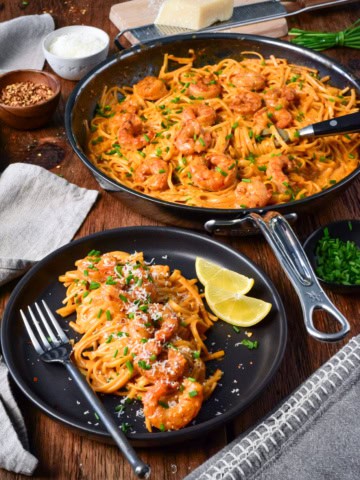 A plate of skillet of creamy spicy Canjun shrimp linguine served with chopped chives and lemon slices.