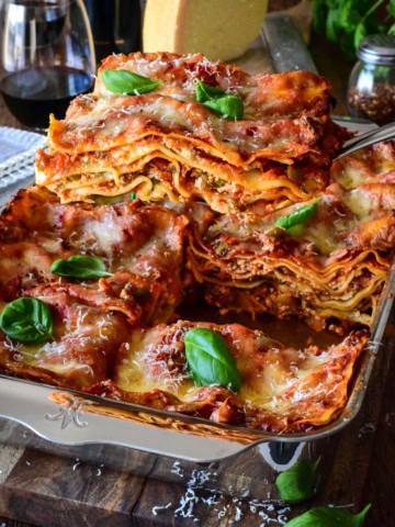 A baking pan with a sausage and beef lasagna and a slice being lifted out to reveal the layers.
