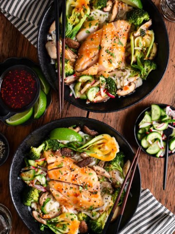 Two bowls of miso black cod served with rice noodles and vegetables.