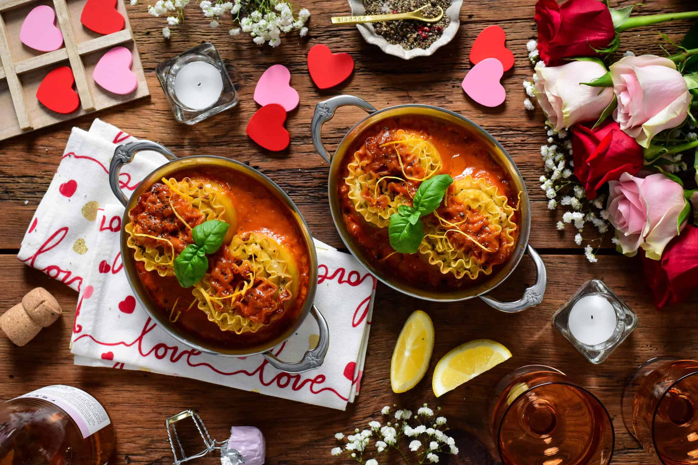 Two individual au gratins, each with two seafood lasagna roll ups served with lemons and rose for Valentine's Day.