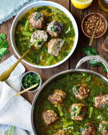 A serving and a pot of chicken ricotta meatballs with lemon orzo brodo, served with grated Parmesan, chili pepper, and a lemon-herb gremolata.