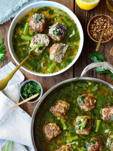 A serving and a pot of chicken ricotta meatballs with lemon orzo brodo, served with grated Parmesan, chili pepper, and a lemon-herb gremolata.