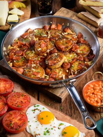 A crispy Irish Pub potato skillet with sausage, bacon and served with sunnyside up eggs, roasted tomatoes and baked beans.